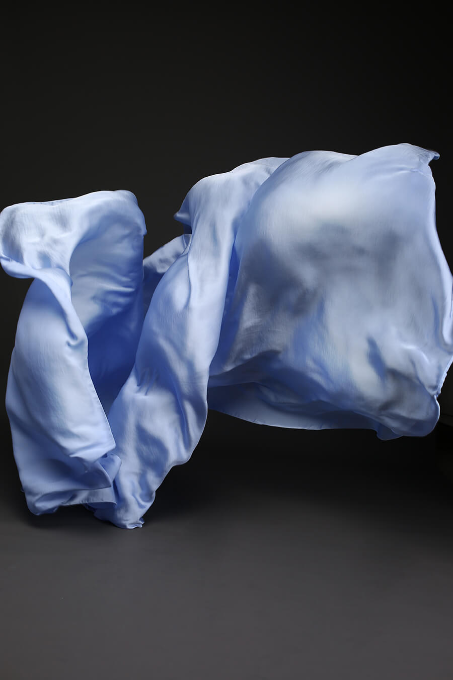 Photo taken on a studio and shows only the mii-estilo silky scarf in light blue color. The photo shows the scarf flying in front of the camera with playful movements.