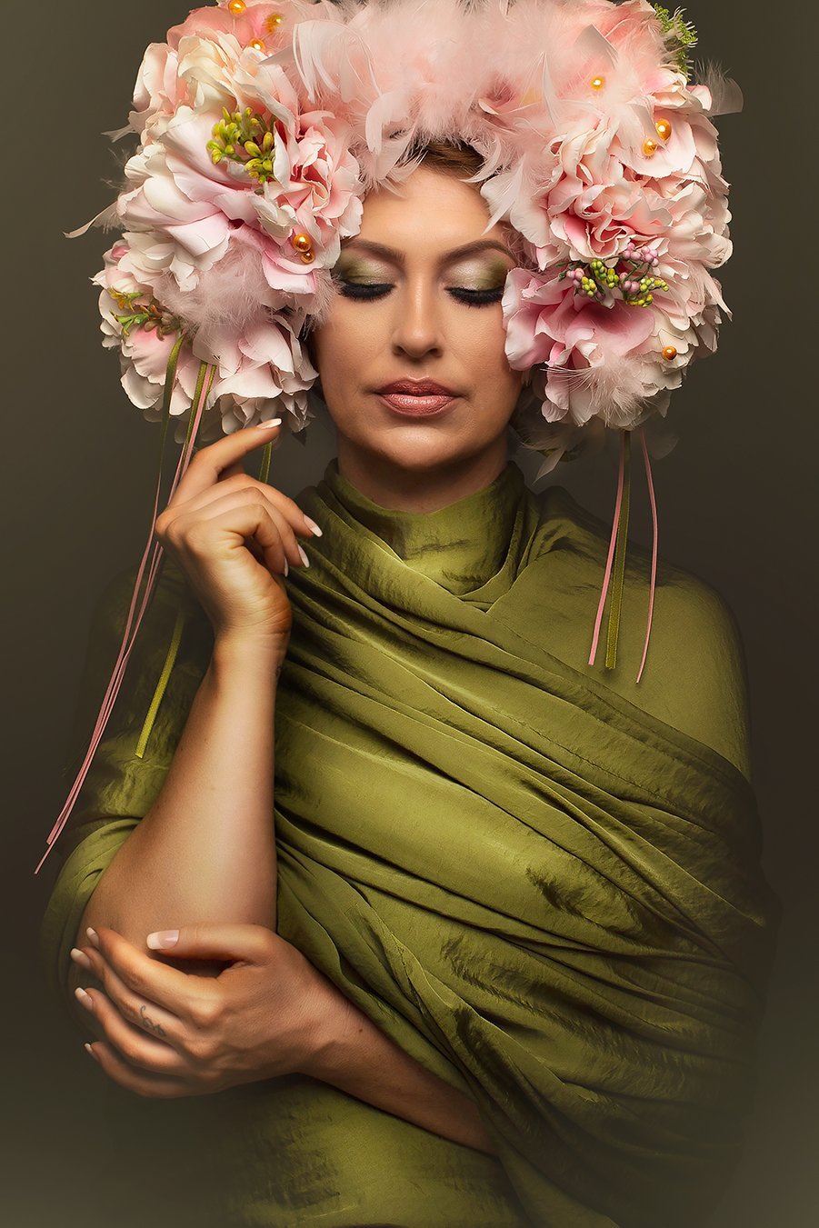 Model with a flower arrangement on her head. Her eyes are closed and she wears a moss green silky scarf on her body. 