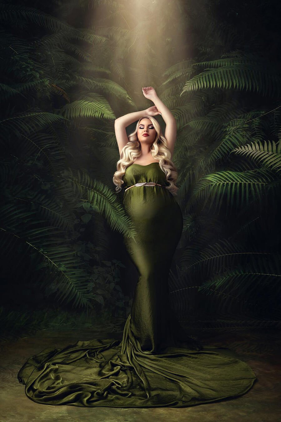 blond model poses next to green plants wearing a moss green silky scarf tied as a dress on her body. there is a sash to tie the scarf on her body.