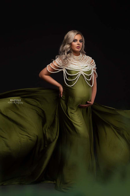A blonde model is posing for the camera. She is wearing a silky scarf moss green as a dress. The sides are going out of the photography. She is wearing a big white pearl necklace on top of it.
