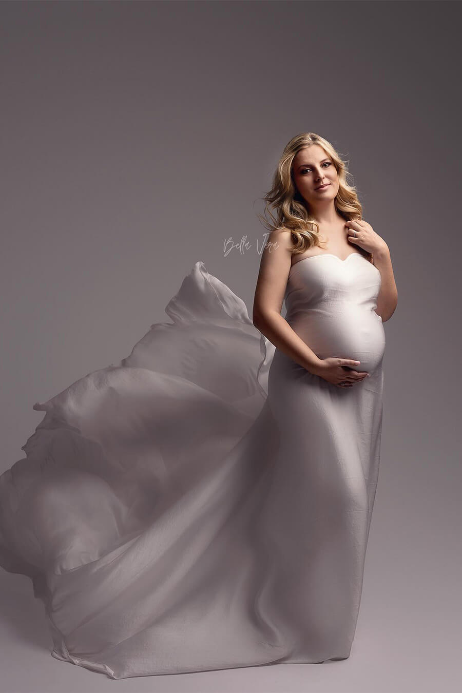 blond pregnant model poses in a studio wearing a off white silky scarf to cover her body.