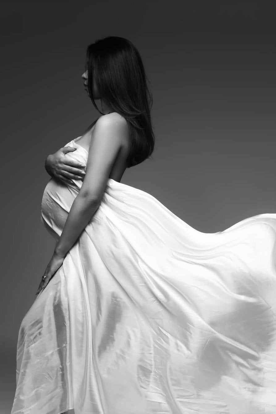 black and white photo of a pregnant woman covering her chest and belly with an off white silky scarf.