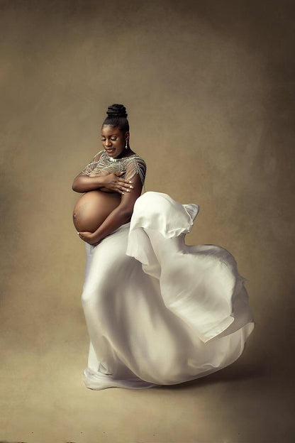 pregnant model poses in a studio during a maternity photoshoot wearing a silky scarf tied on her waist and a big silver necklace.