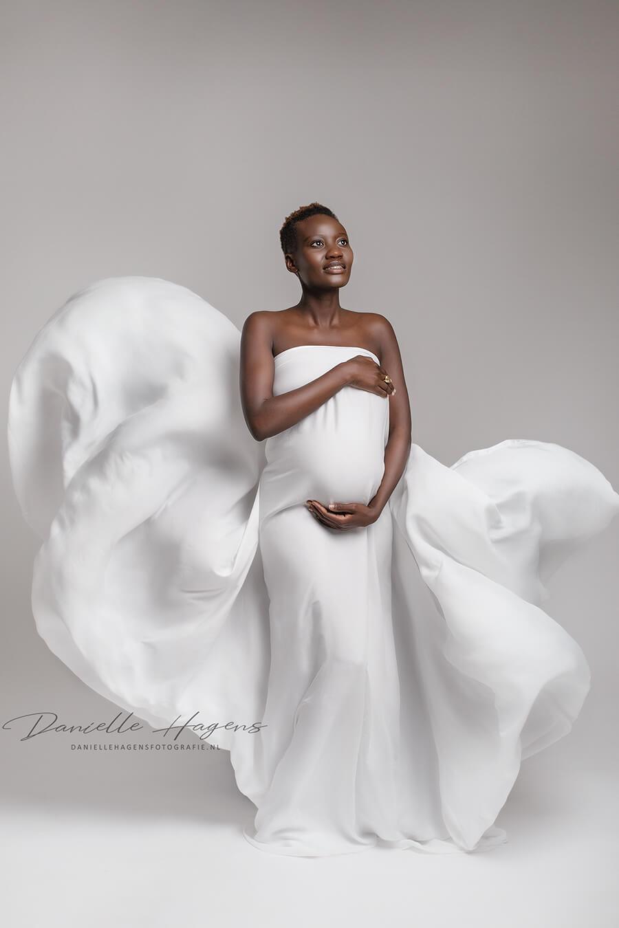 pregnant model poses covering her body with a silky scarf in off white.