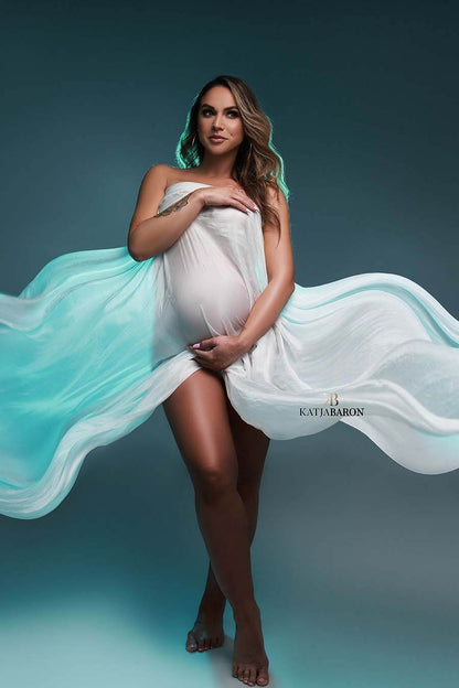 pregnant model poses with a blue background wearing a scarf in off white to cover her body.