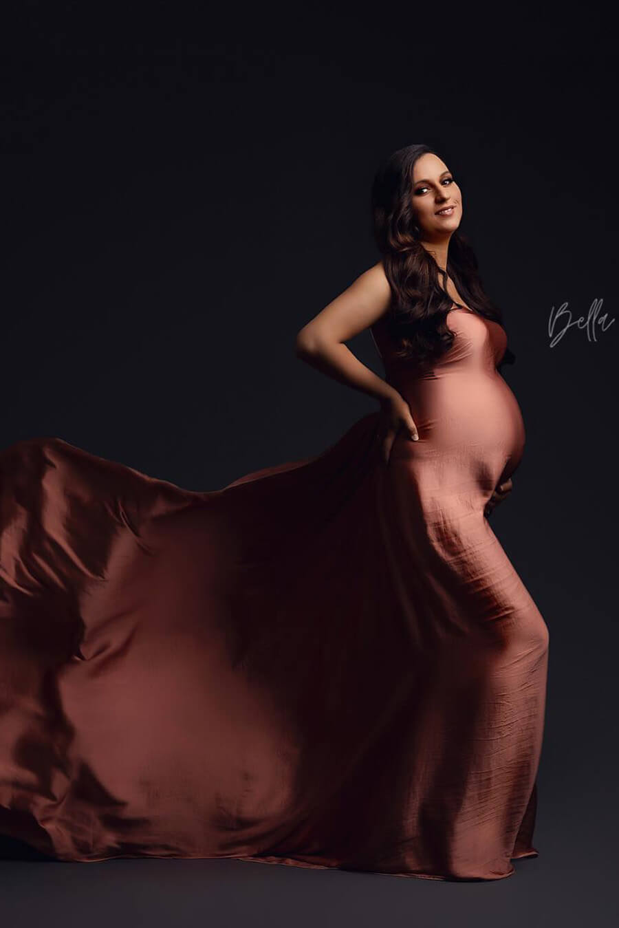 brunette pregnant model poses in a studio wearing a silky scarf wrapped around her body.