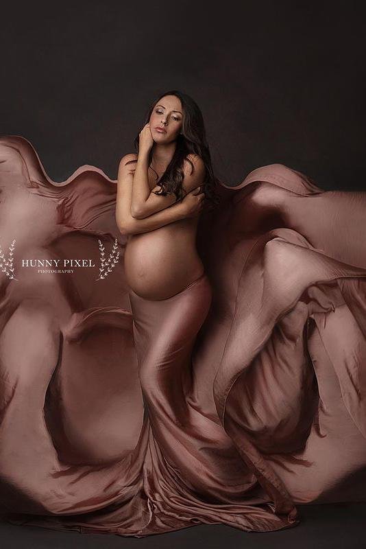 Brunette model poses in a studio with a piece of old pink silky fabric tied to her waist. She covers her chest with both hands and has her eyes partially open.