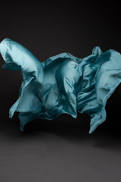 Photo taken on a studio and shows only the mii-estilo silky scarf in powder blue color. The photo shows the scarf flying in front of the camera with playful movements.