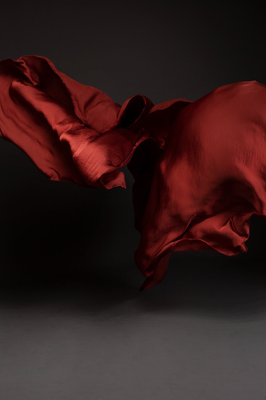 Photo taken on a studio and shows only the mii-estilo silky scarf in rust orange color. The photo shows the scarf flying in front of the camera with playful movements.
