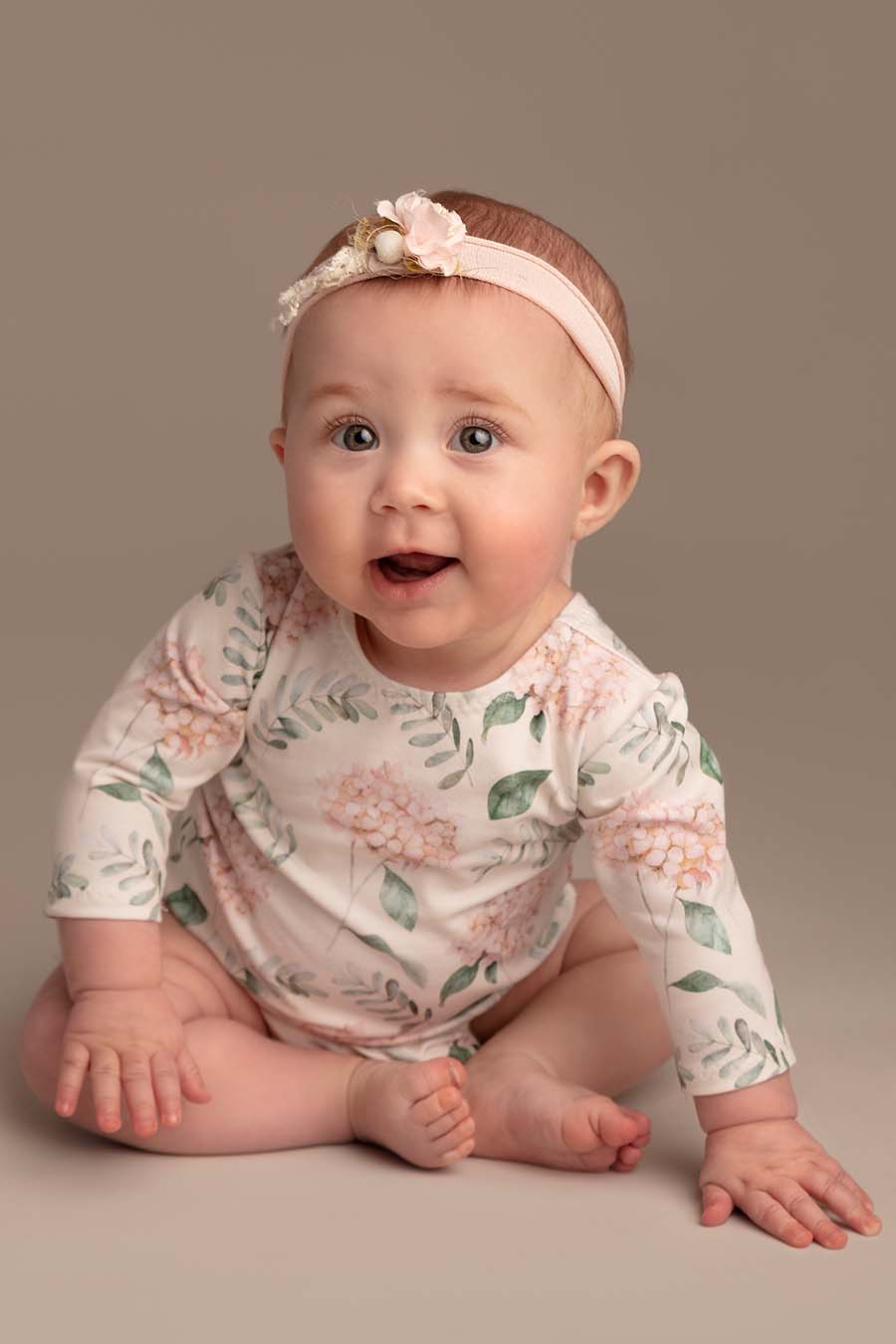 baby poses wearing a romper with long sleeves and flower pattern. she has a matching hairband.