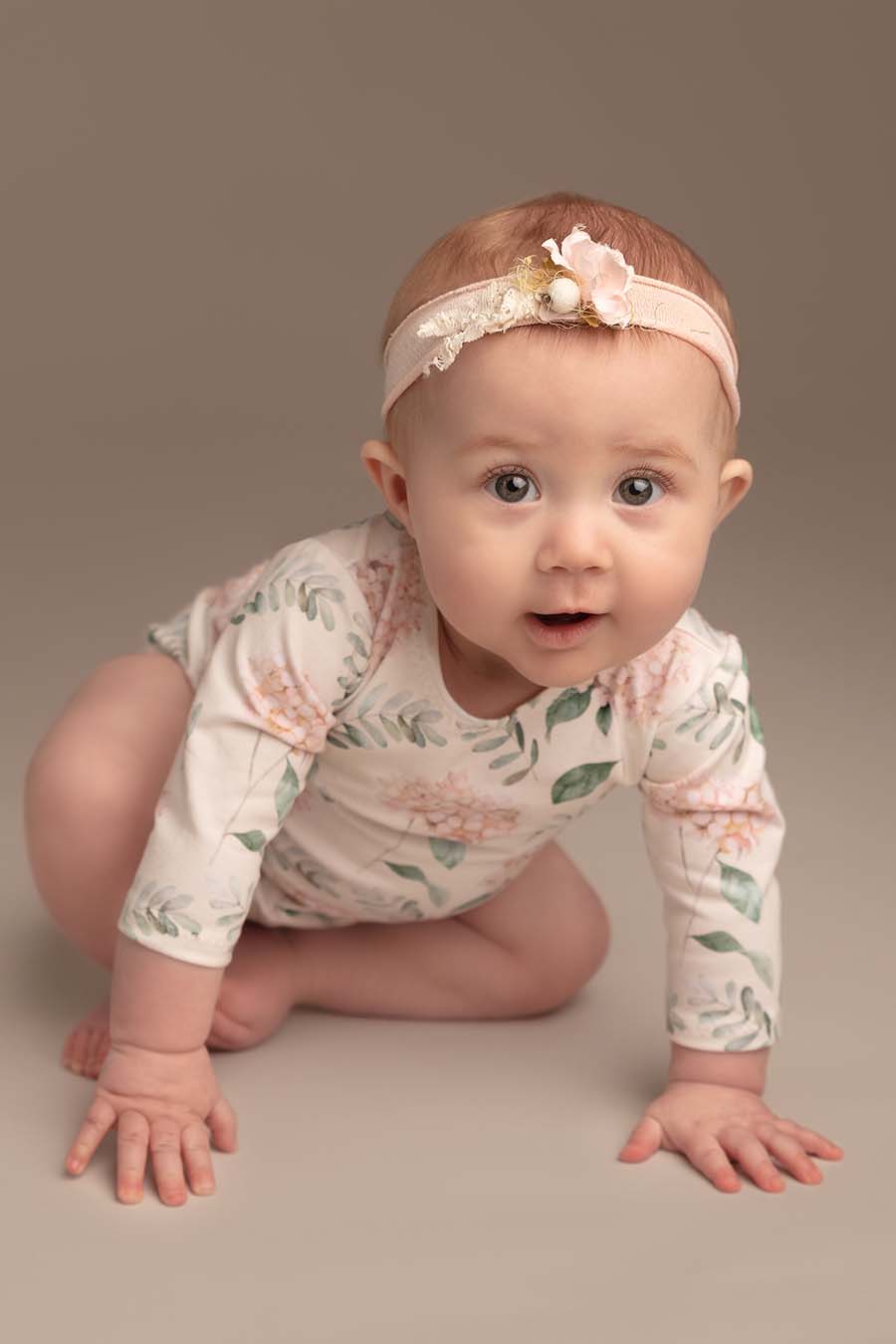 baby poses wearing a romper with long sleeves and flower pattern. she has a matching hairband.