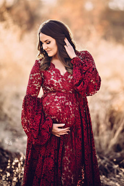 A maternity model is standing outside. she is wearing a bordeaux dress. the dress is from lace. The model is looking down at the ground