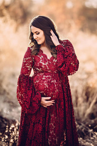 A maternity model is standing outside. she is wearing a bordeaux dress. the dress is from lace. The model is looking down at the ground