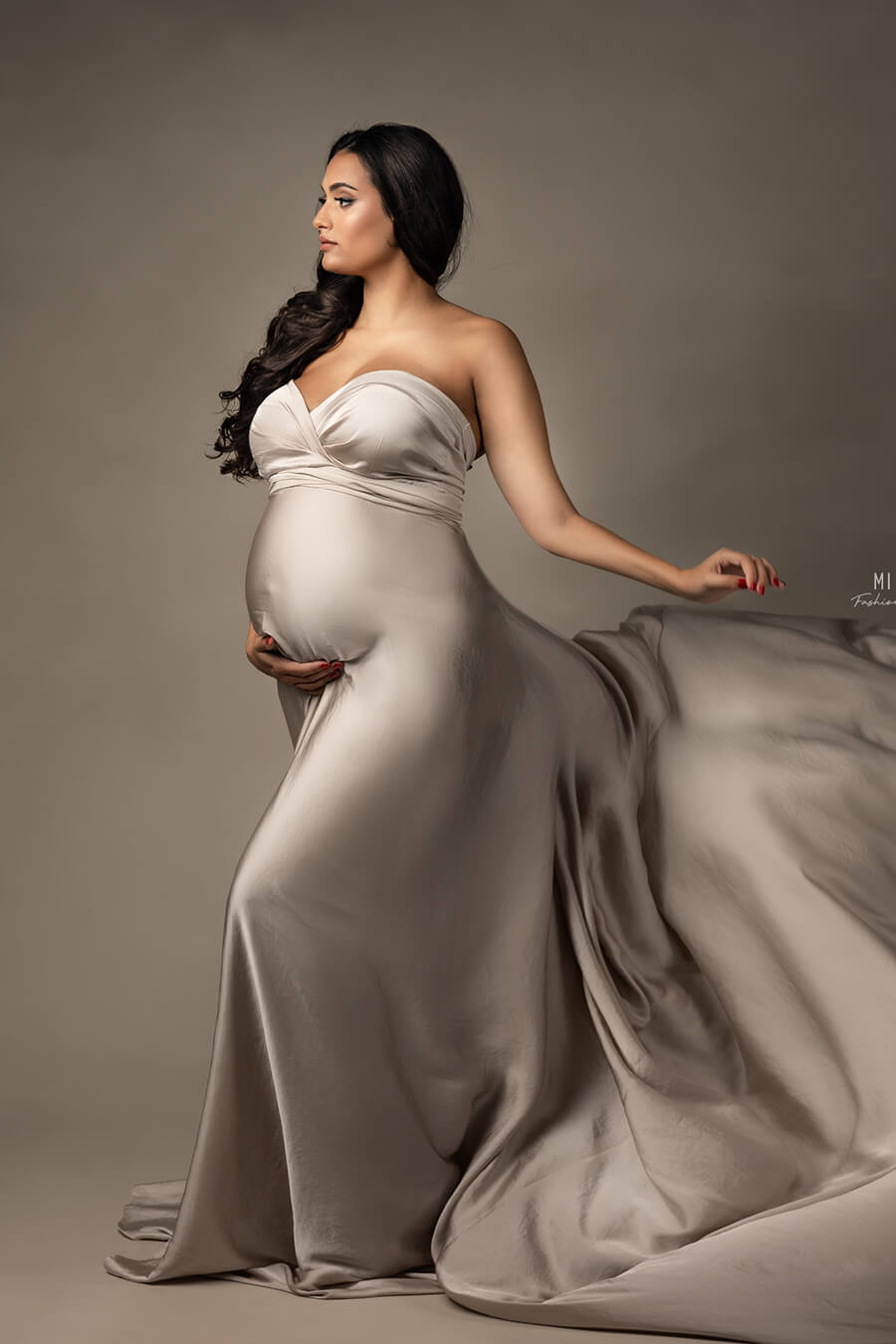 brunette model poses in a studio wearing a draping silky fabric in sand color wrapped as a dress.